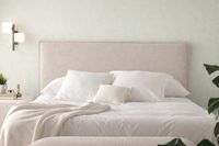 CARTIER upholstered headboard in natural beige fabric with removable cover, styled with white bedding against a soft sage wall i CARTIER upholstered headboard in natural beige fabric with removable cover, styled with white bedding against a soft sage wall i